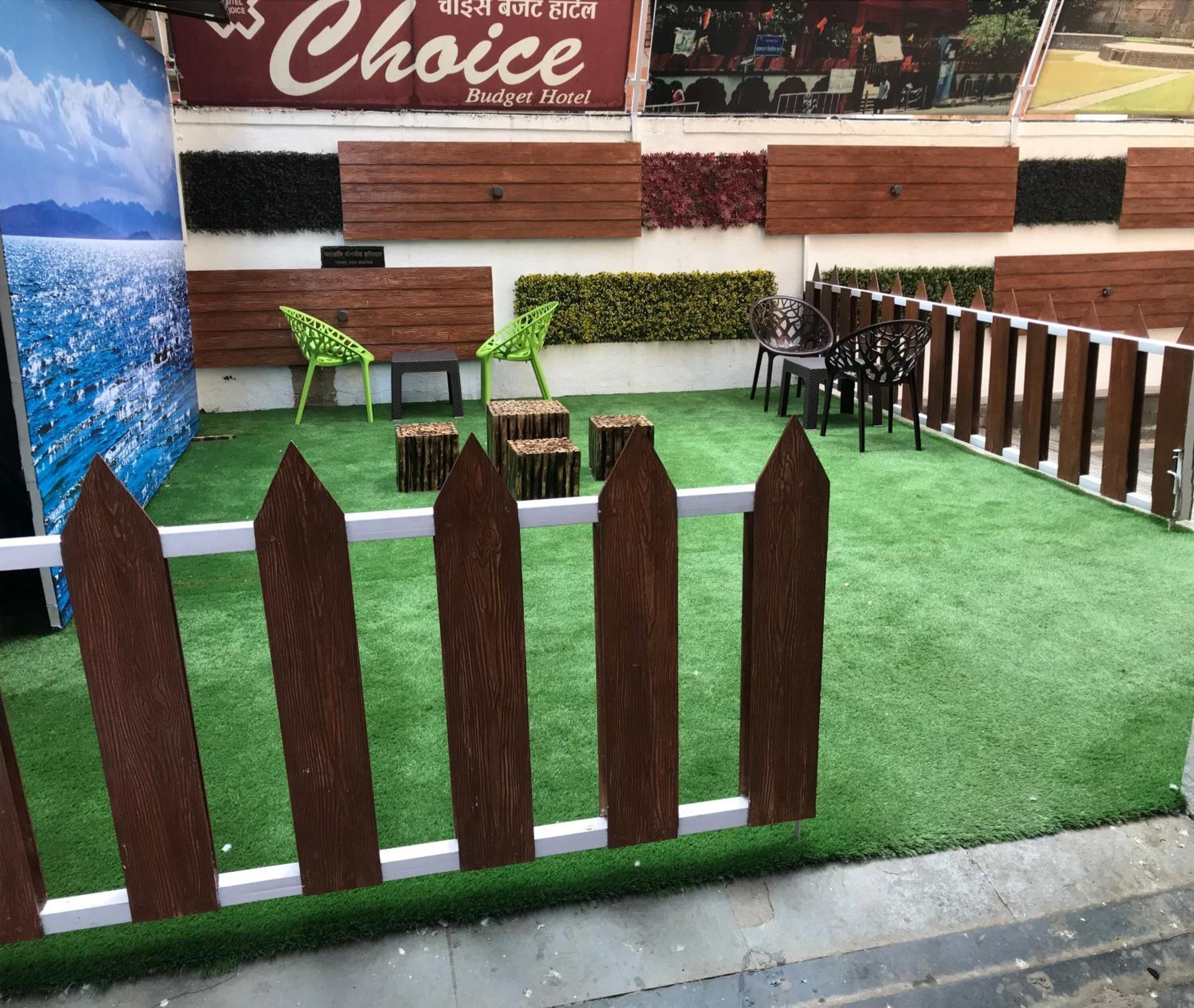 A courtyard with artificial grass, wooden fence, and outdoor seating area with chairs and tables.