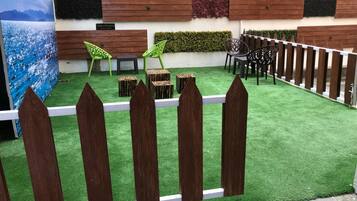 A courtyard with artificial grass, wooden fence, and outdoor seating area with chairs and tables.