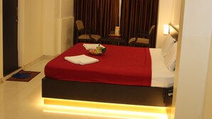 A hotel room with a bed, a desk, two chairs, a nightstand, and an air conditioning unit. - Choice Classic Hotel (Pune)