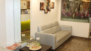 A modern living room with a grey sofa, a coffee table with a plate of food and drinks, and a large floral painting on the wall. - Choice Classic Hotel (Pune)