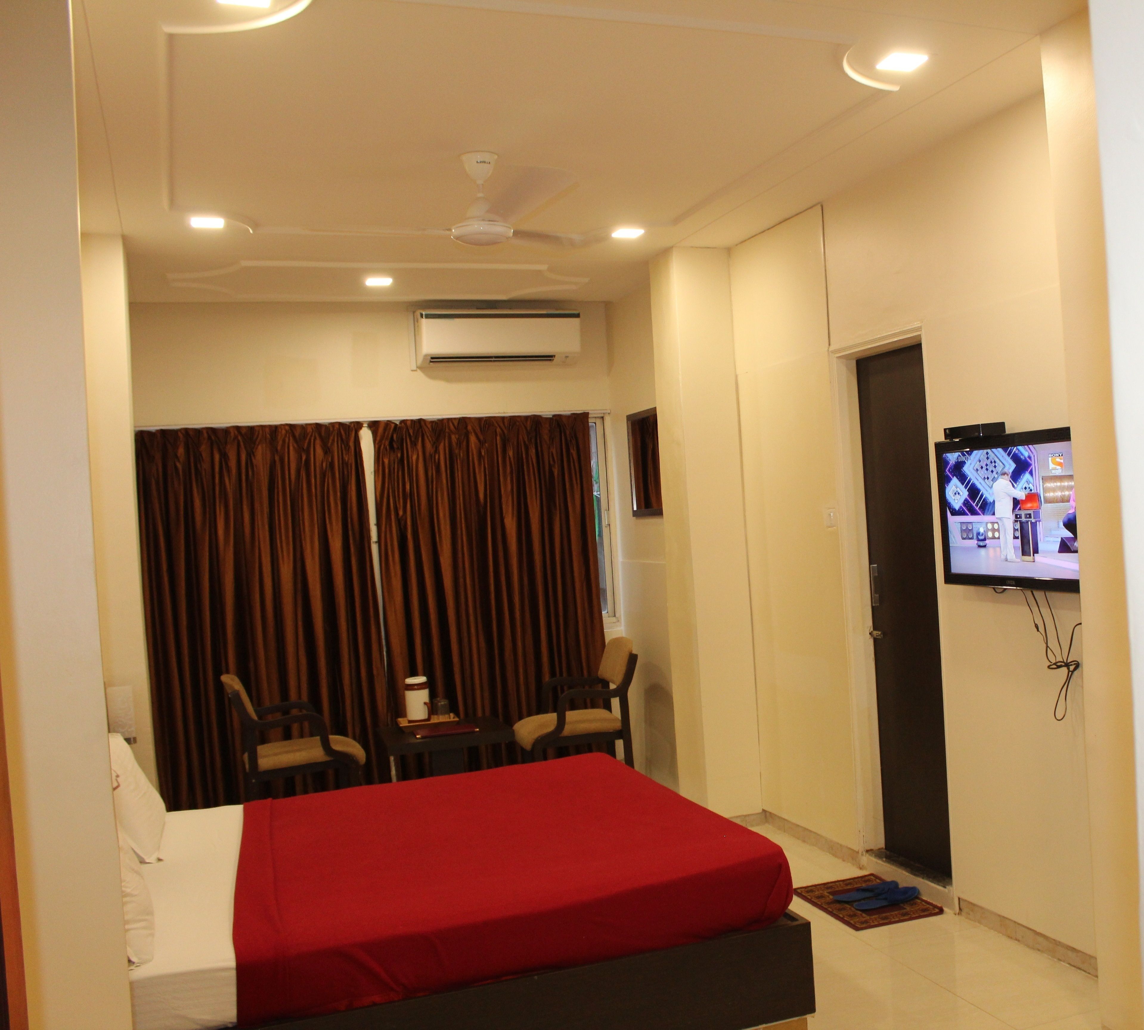 A hotel room with a bed, a TV mounted on the wall, a ceiling fan, and an air conditioning unit.