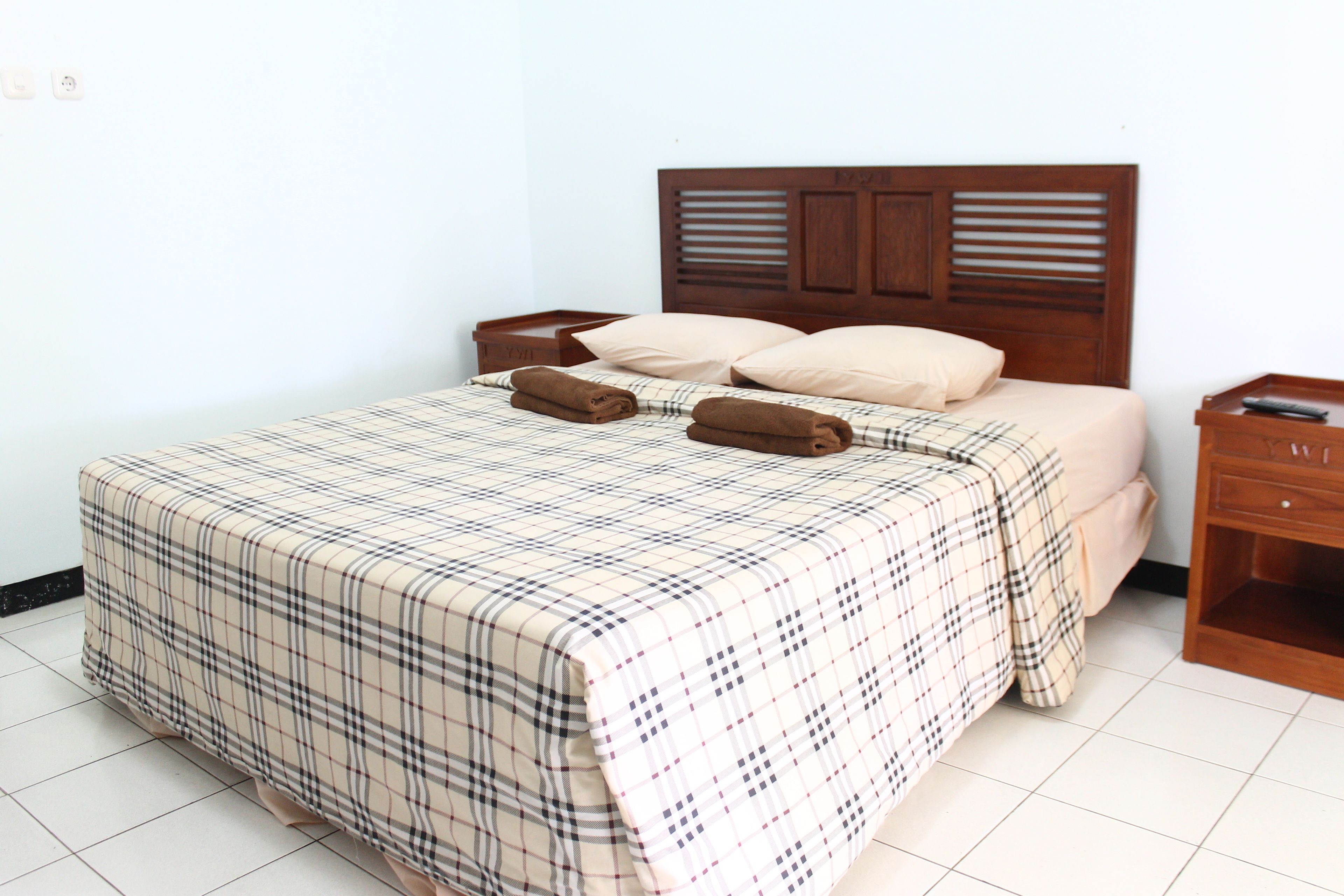 A neatly made bed with a plaid bedspread, two pillows, and two rolled towels.