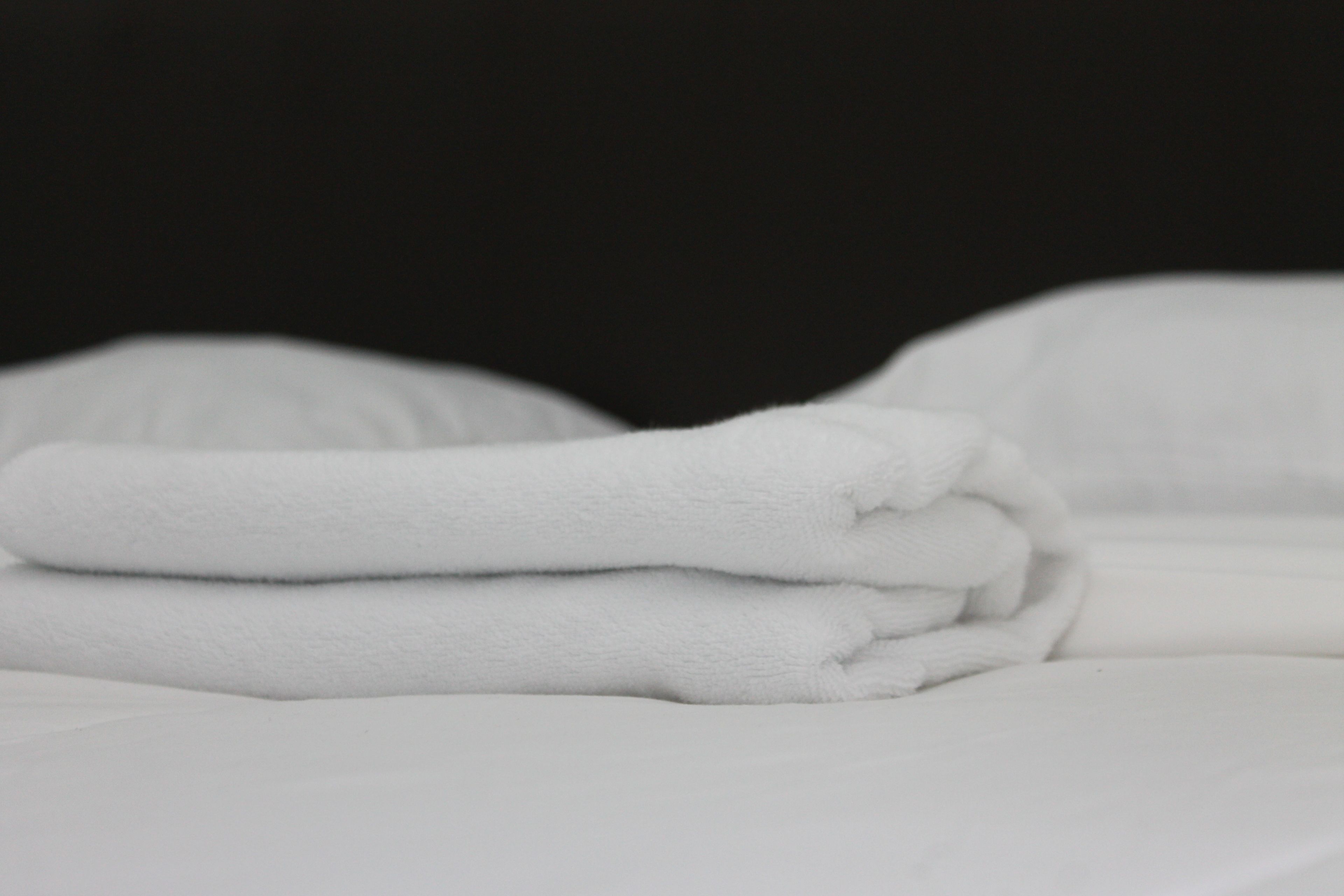 Toalha branca dobrada cuidadosamente sobre a cama com roupa de cama branca.