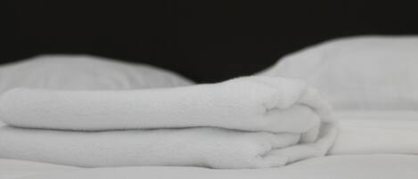 Un asciugamano bianco piegato ordinatamente su un letto con lenzuola bianche.