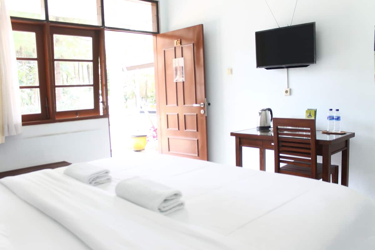 Habitación de hotel con cama, escritorio, silla, televisor y ventana con cortinas.