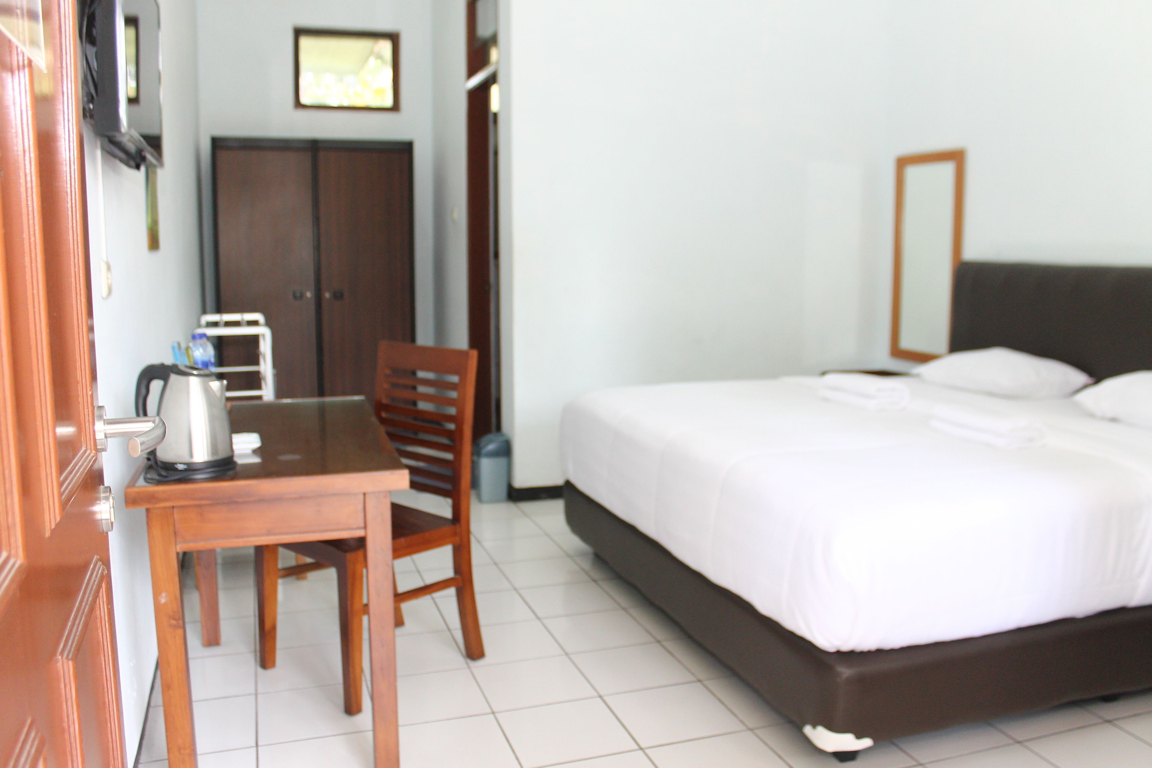 A hotel room with a bed, a desk with a chair, a wardrobe, and a television on the wall.