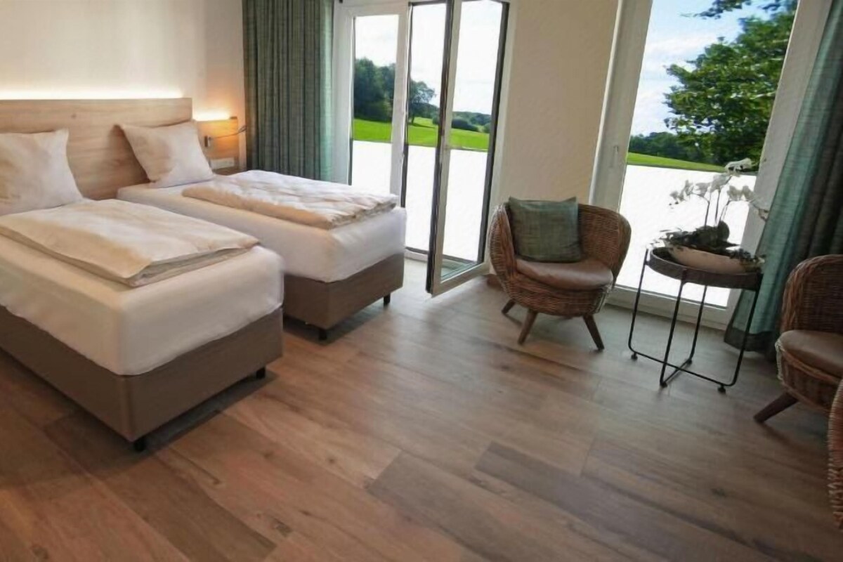 A hotel room with two beds, a nightstand, a chair, and a view of the outdoors.
