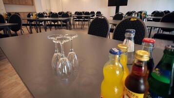 A conference room with tables and chairs, a large table with wine glasses, and bottles of beverages.