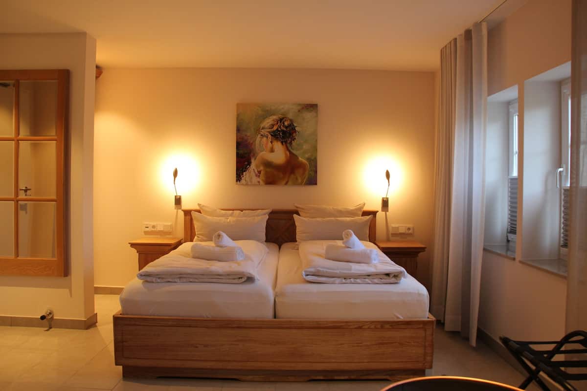 Una cama doble con dos mesitas de noche, un cuadro en la pared y una ventana con cortinas.