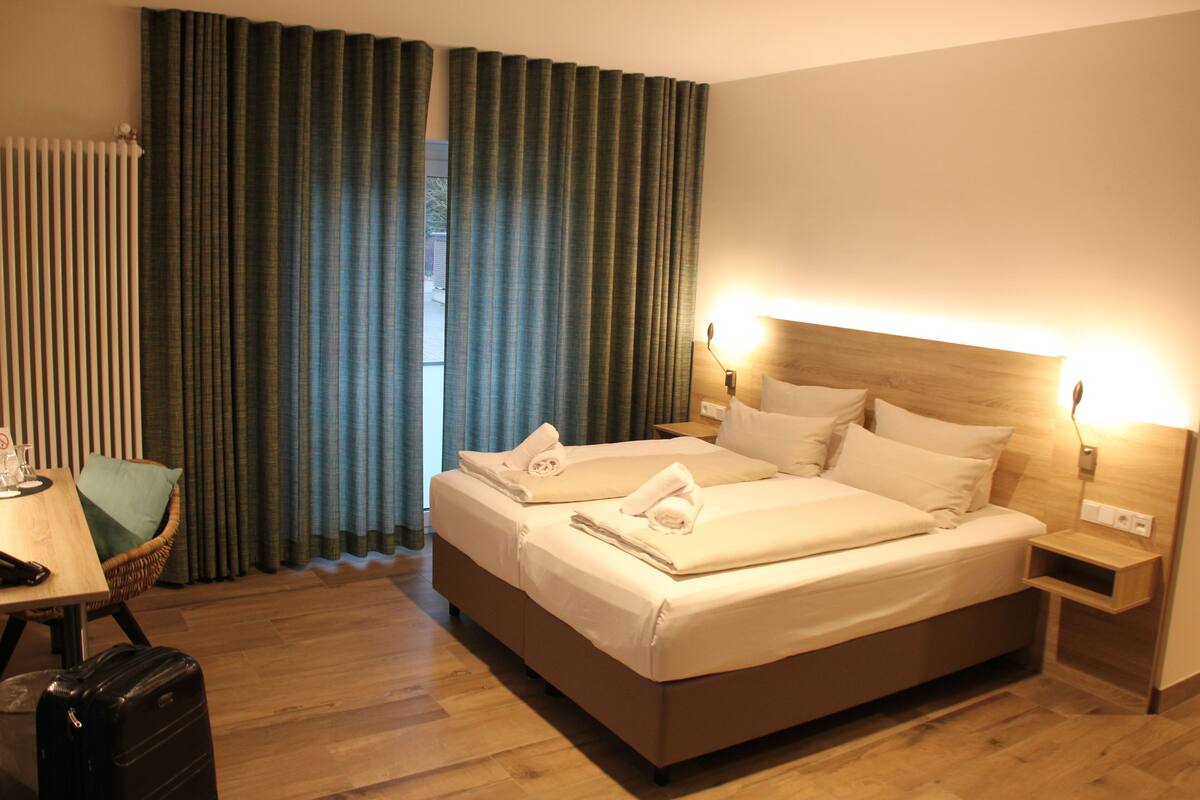 Una habitación de hotel con una cama grande, mesitas de noche, una silla y una maleta.