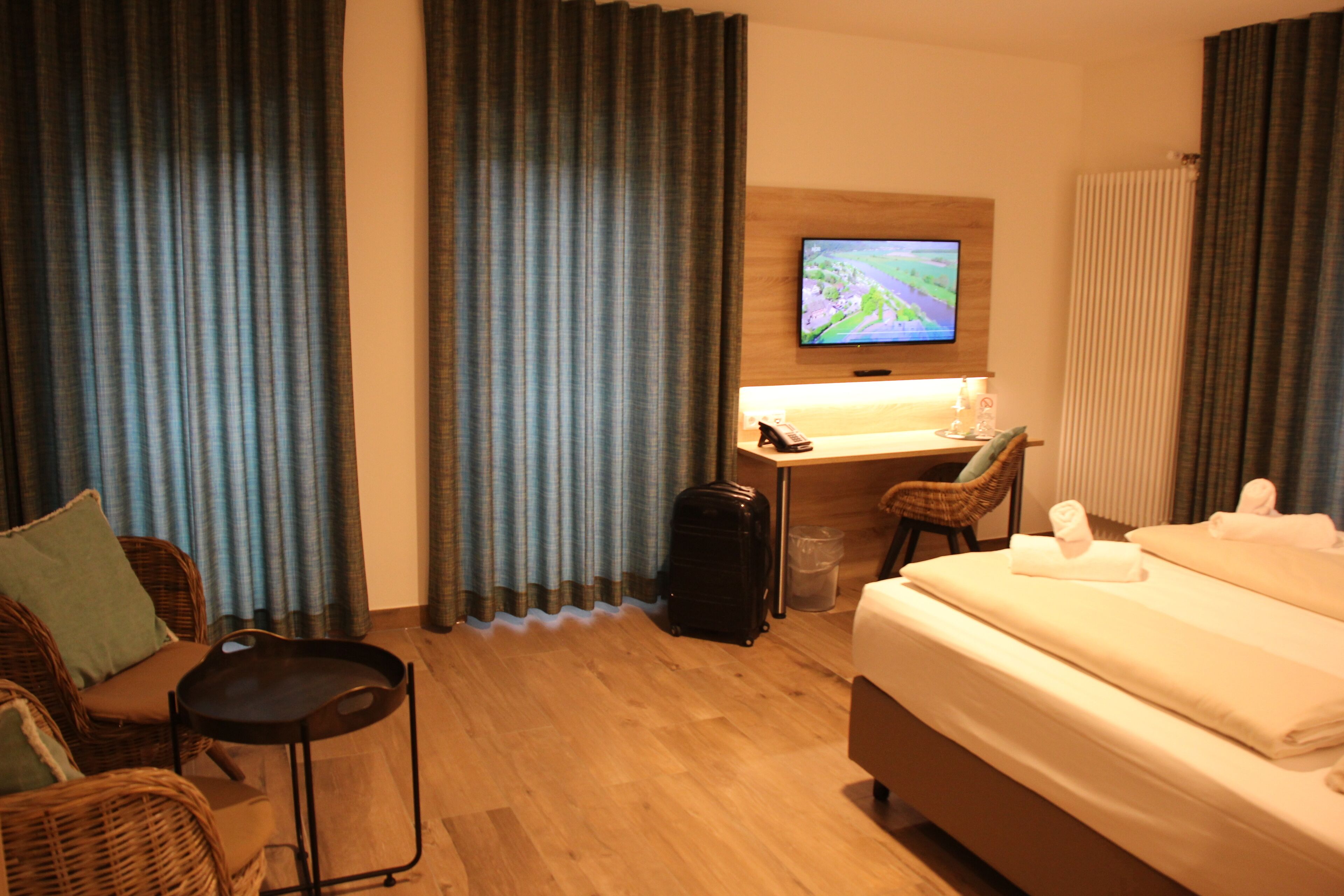 A hotel room with a bed, a desk with a computer, a chair, a suitcase, and a television on the wall.