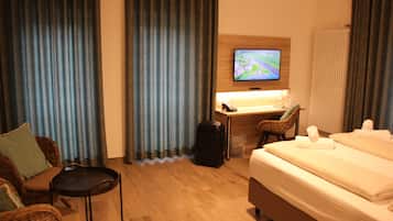 A hotel room with a bed, a desk with a computer, a chair, a suitcase, and a television on the wall.