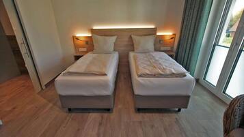 A hotel room with two beds, a wooden floor, and a large window with curtains.