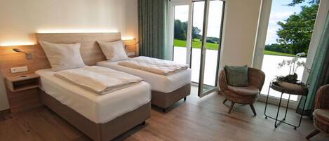 A double room with two beds, a nightstand, a chair, and a view of a green landscape through a glass door.