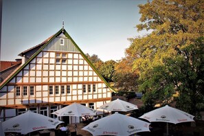 Un edificio tradicional con entramado de madera, con mesas al aire libre y sombrillas con el logotipo de Weissbier.