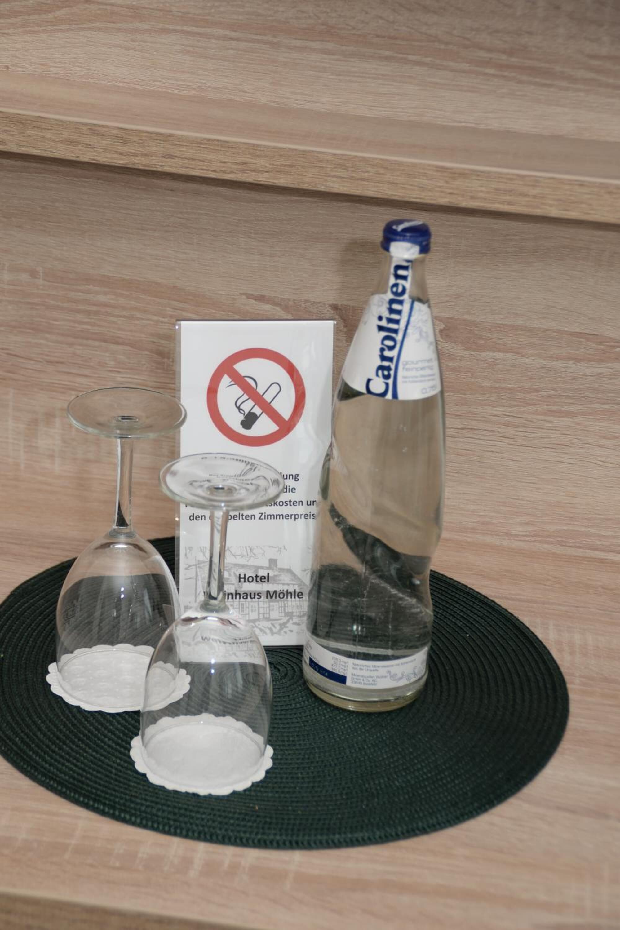 A bottle of Carolin, a glass with a coaster, and a no-smoking sign on a placemat.