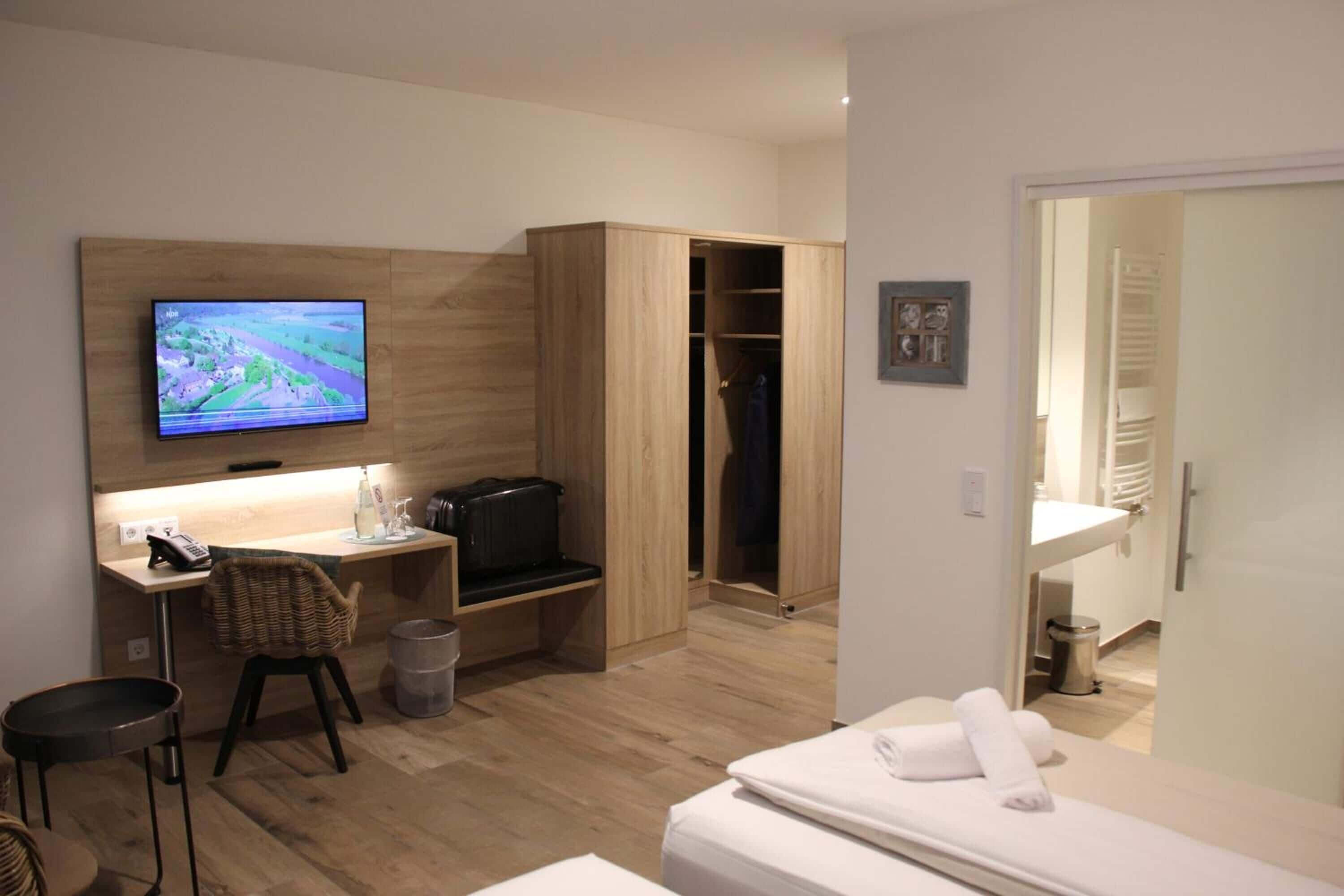 A hotel room with a wooden desk, a television, a wardrobe, and a bed with towels.