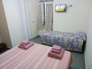Ein Hotelzimmer mit zwei Betten, jeweils mit rosafarbenen Handtüchern, einem an der Wand befestigten Fernseher und einem Fenster mit Vorhängen.