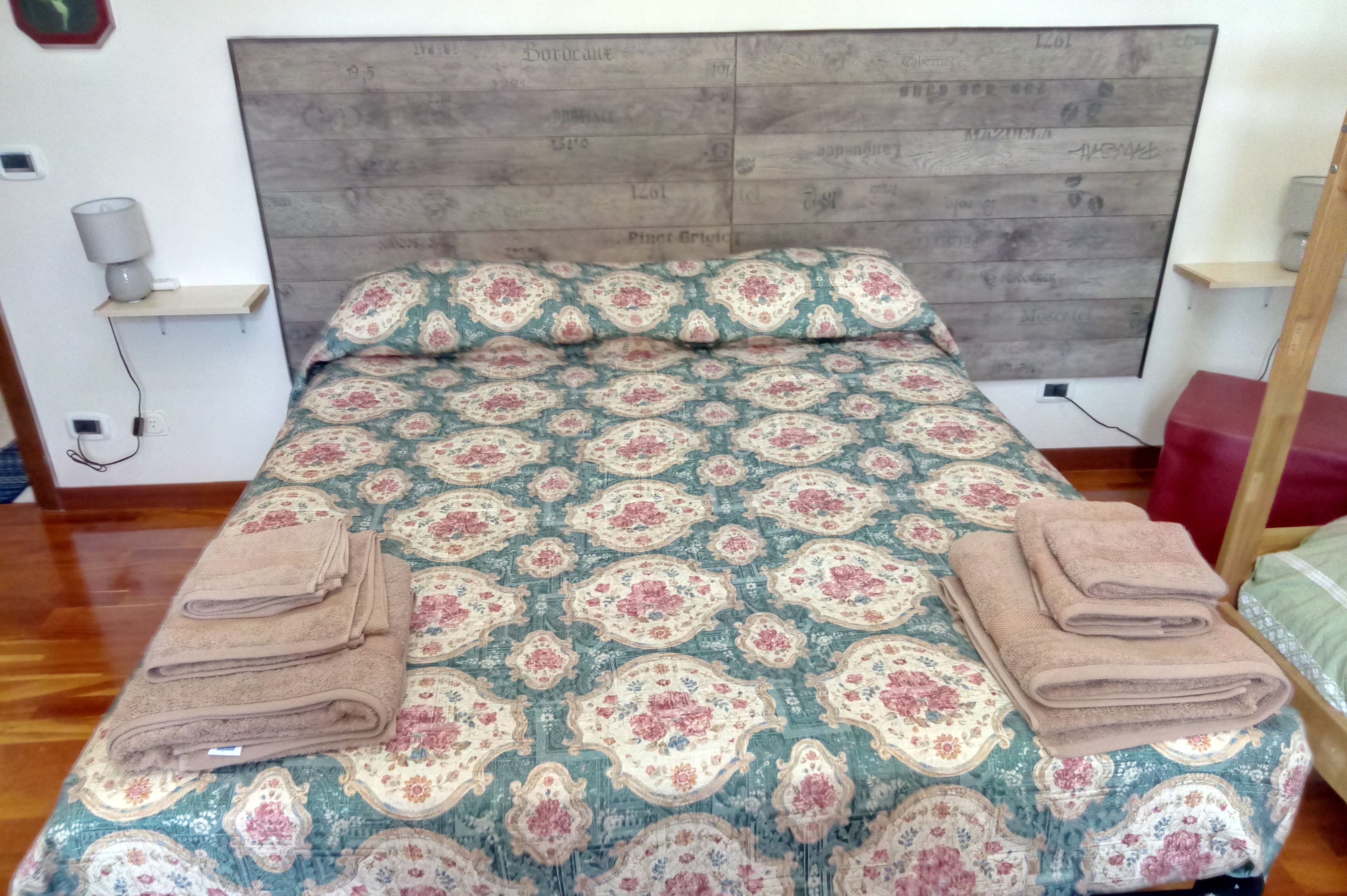 A neatly made bed with a patterned bedspread and two folded towels on the side.