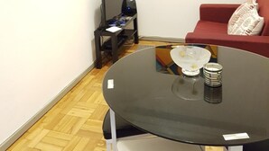 A modern living room with a round glass table, a red sofa, and a wall-mounted abstract painting. - Apartamento À Cedofeita (Porto)
