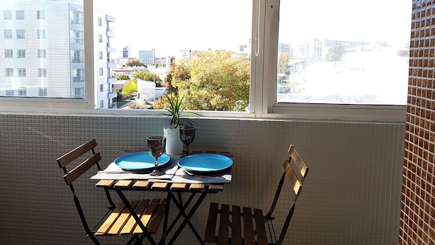 A dining table with blue plates and a glass, set against a tiled wall with a window overlooking a cityscape. - Apartamento À Cedofeita (Porto)