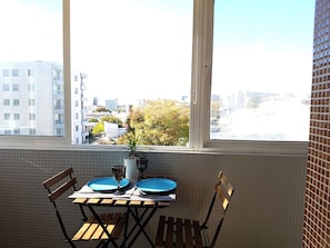 A dining table with blue plates and a glass, set against a tiled wall with a window overlooking a cityscape. - Apartamento À Cedofeita (Porto)