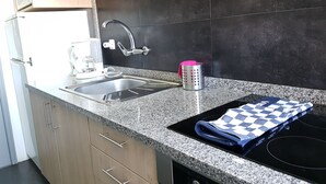 A kitchen with a granite countertop, stainless steel sink, and a black stovetop. - Apartamento À Cedofeita (Porto)