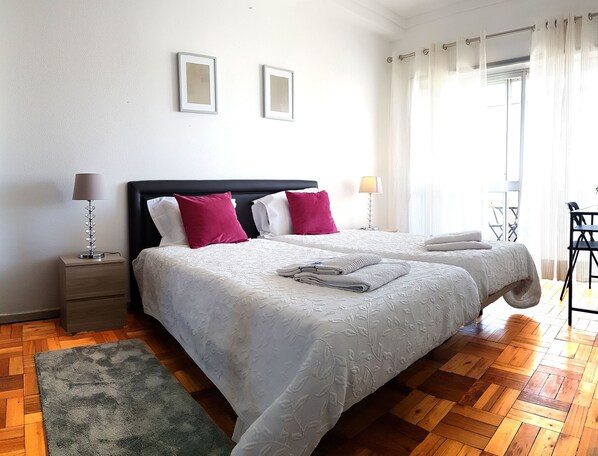 A double bed with white bedding and two pillows, a nightstand with a lamp, a green rug, and a wooden floor. - Apartamento À Cedofeita (Porto)