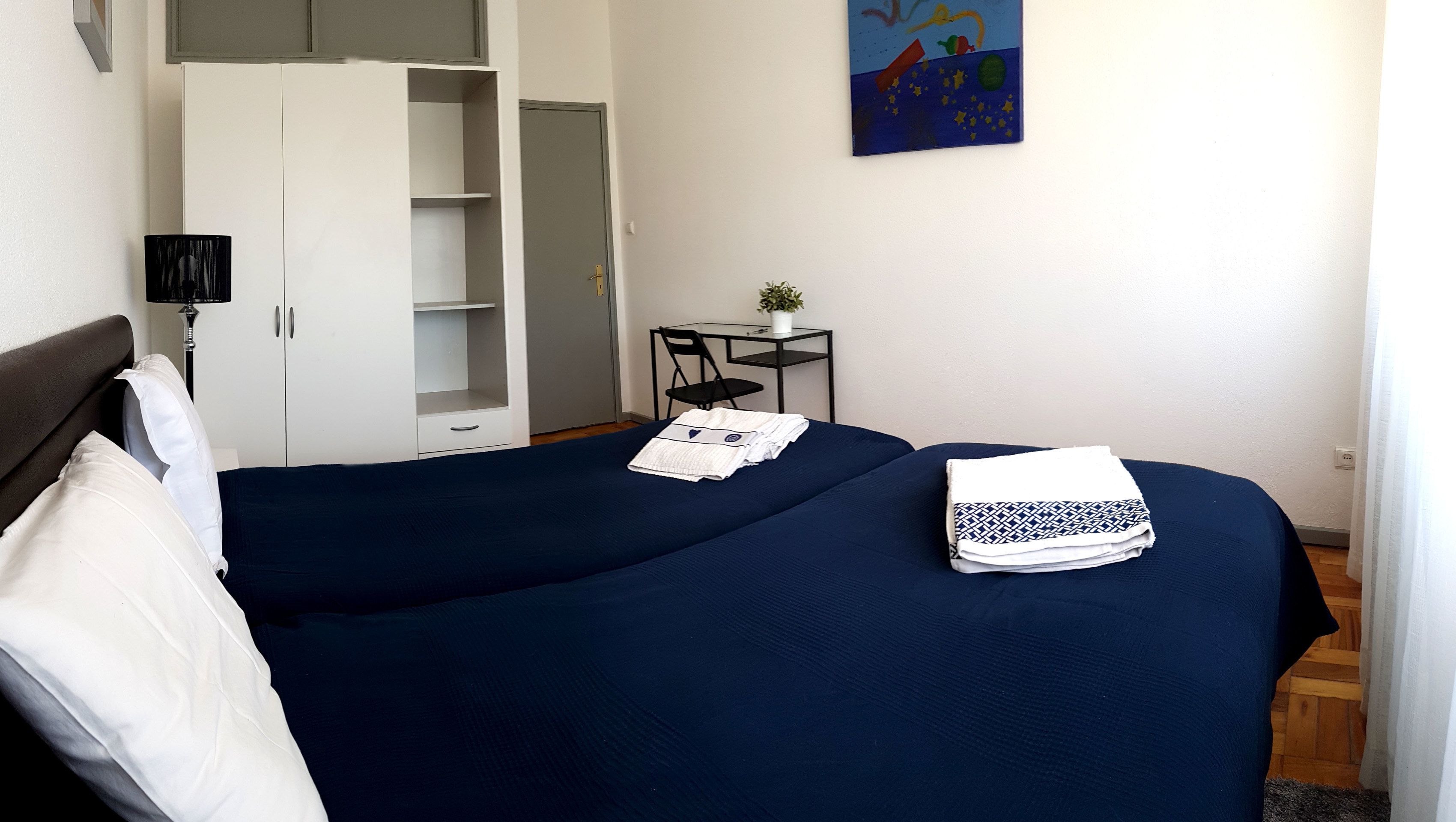 Une chambre à coucher avec un lit, une armoire, un bureau et un tableau accroché au mur.