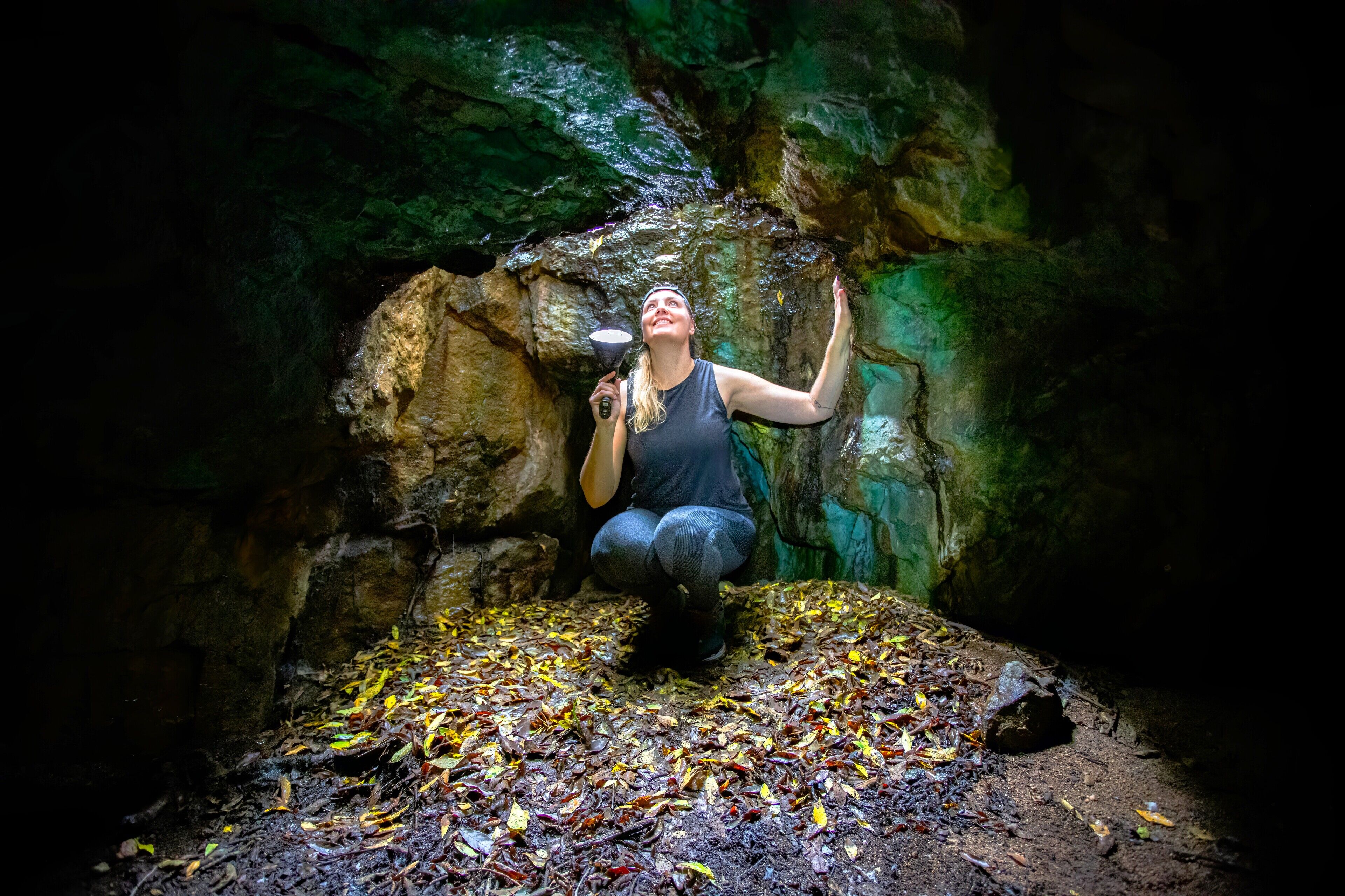 Una persona en una cueva con paredes rocosas y el suelo cubierto de hojas.
