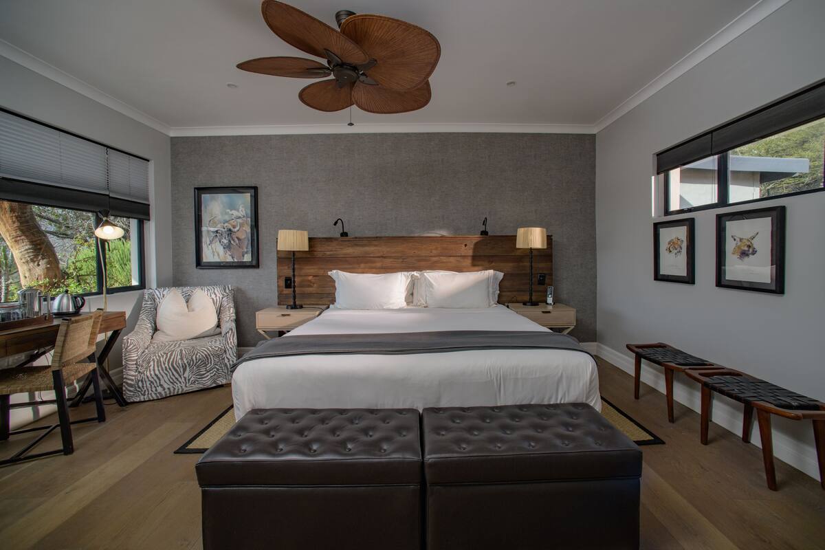 A modern bedroom with a large bed, a ceiling fan, a desk with a chair, and artwork on the walls.