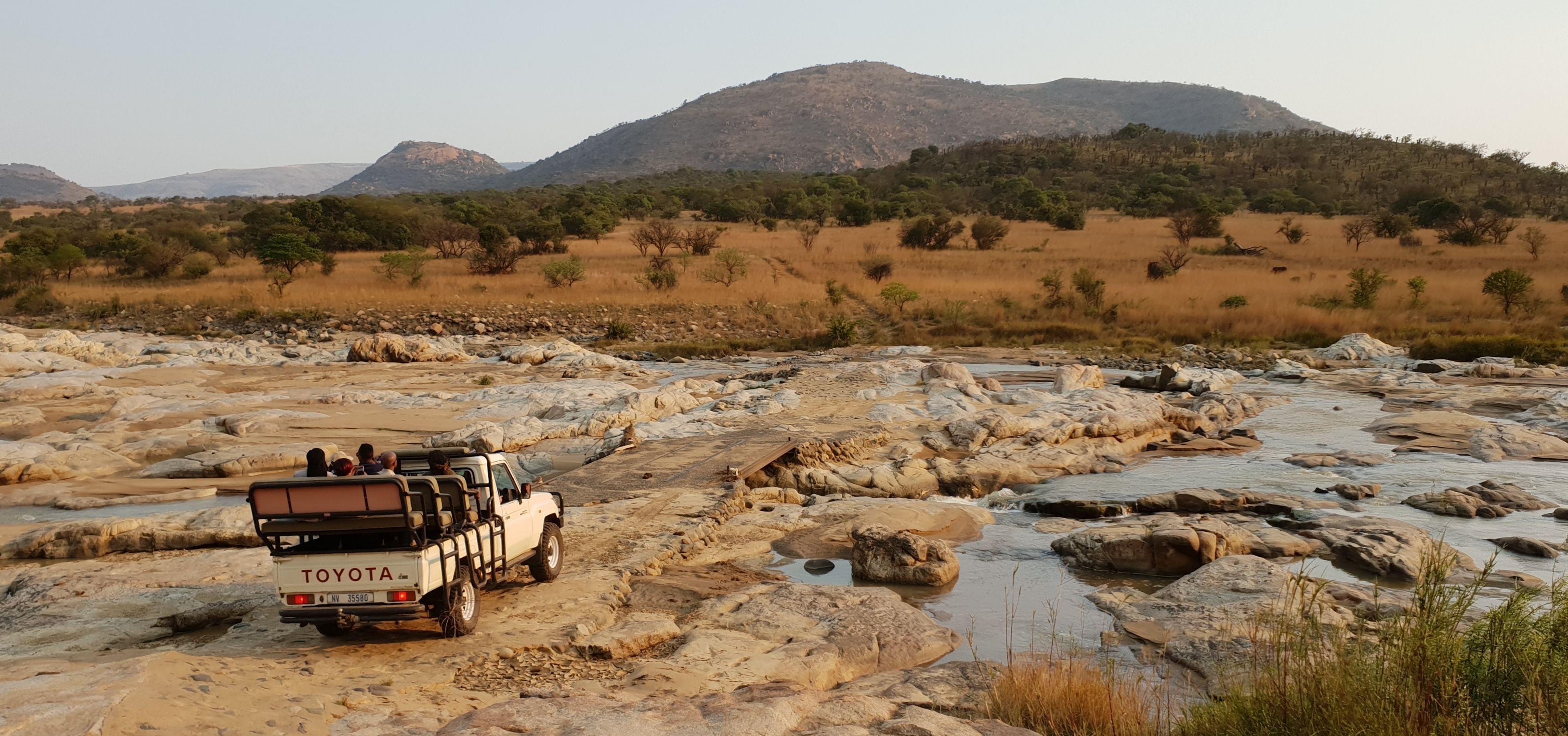 Un SUV Toyota estacionado sobre terreno rocoso, con un río y montañas al fondo.