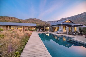 A modern house with a swimming pool, surrounded by a wooden deck and lush vegetation. - Valley Lodge - Babanango Game Reserve (Ulundi)