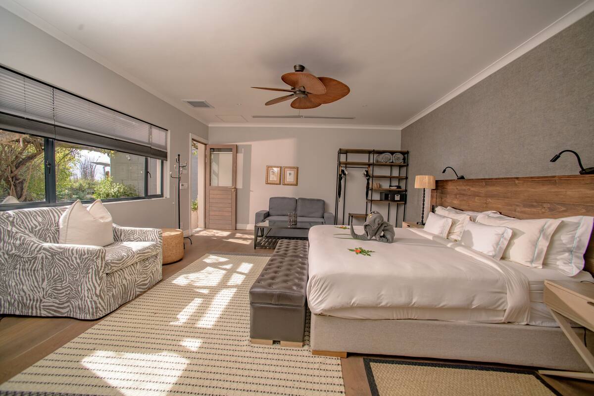 A modern bedroom with a large bed, a sofa, a chair, and a ceiling fan.