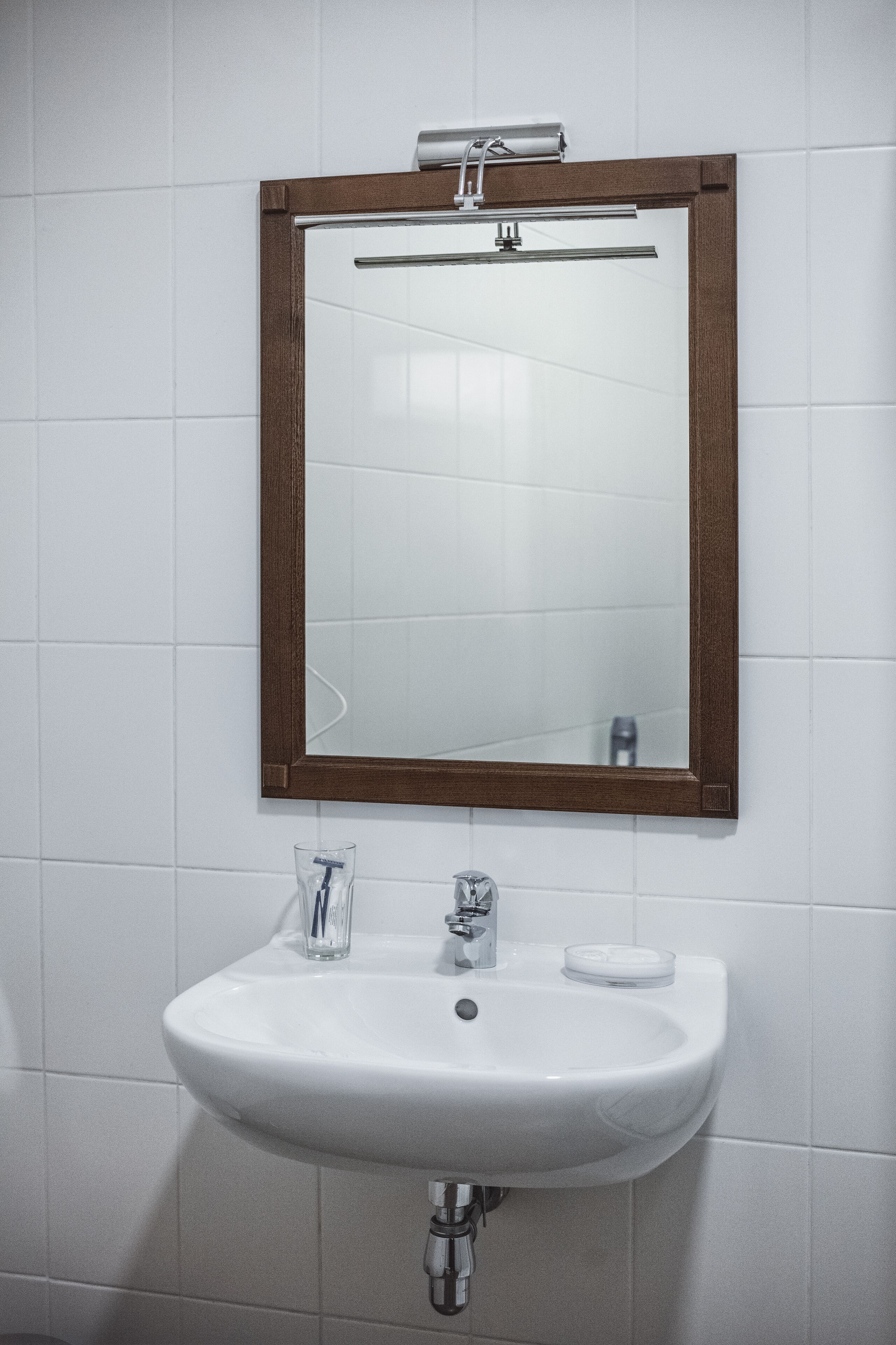 A bathroom with a white sink, a mirror with a wooden frame, and a towel rack above the mirror.