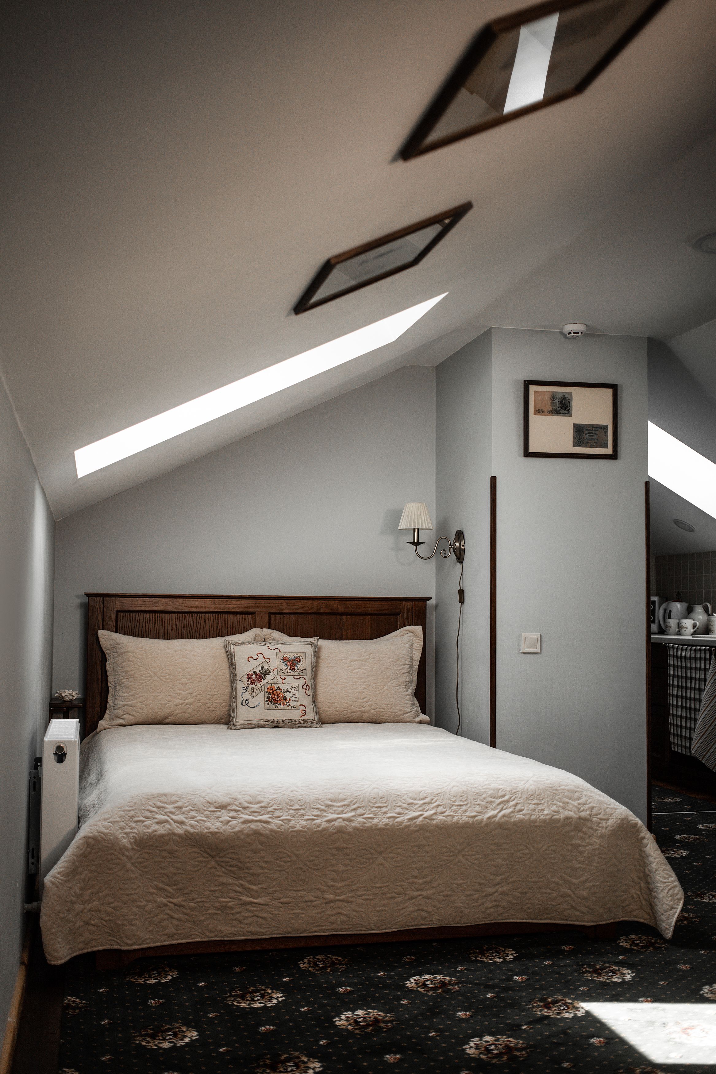 A bedroom with a large bed, a headboard, a nightstand, a wall-mounted lamp, and a ceiling light.