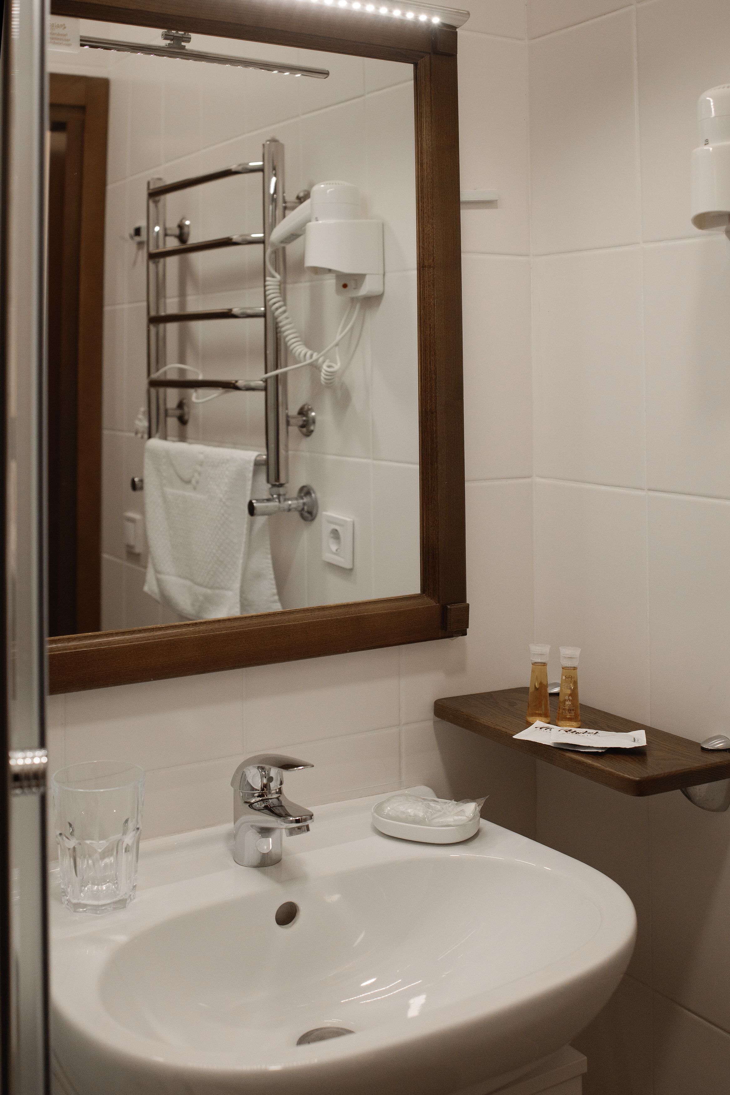 A bathroom with a sink, mirror, towel rack, and a shelf with toiletries.