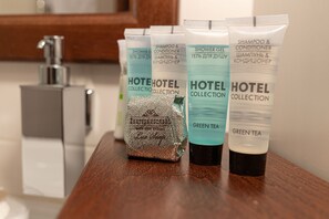 Una encimera de baño con diversos artículos de tocador de la colección del hotel, incluyendo champú, acondicionador y té verde.