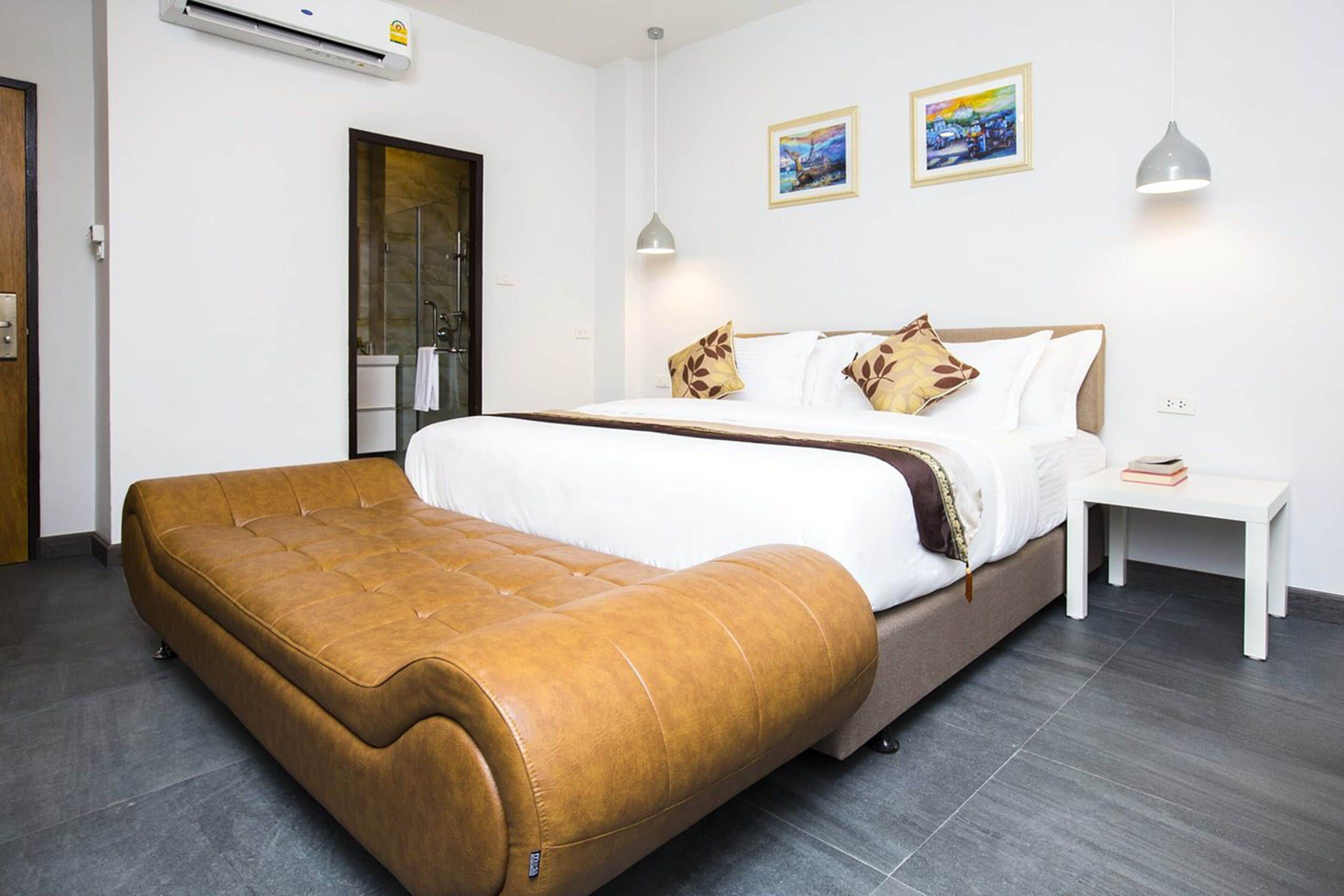 A modern hotel room with a large bed, a brown leather sofa, a small bedside table, and two wall-mounted lamps.