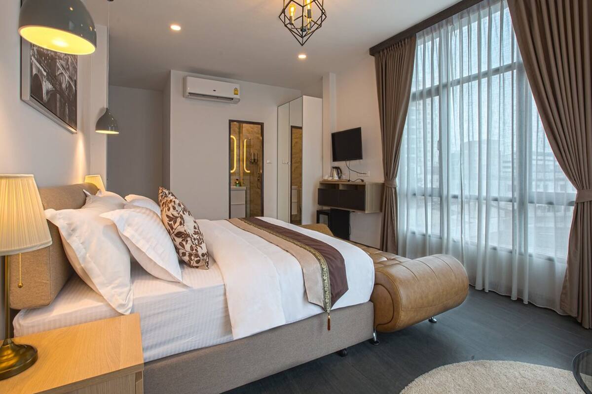 Een moderne hotelkamer met een groot bed, een nachtkastje met een lamp, een televisie en een groot raam met gordijnen.