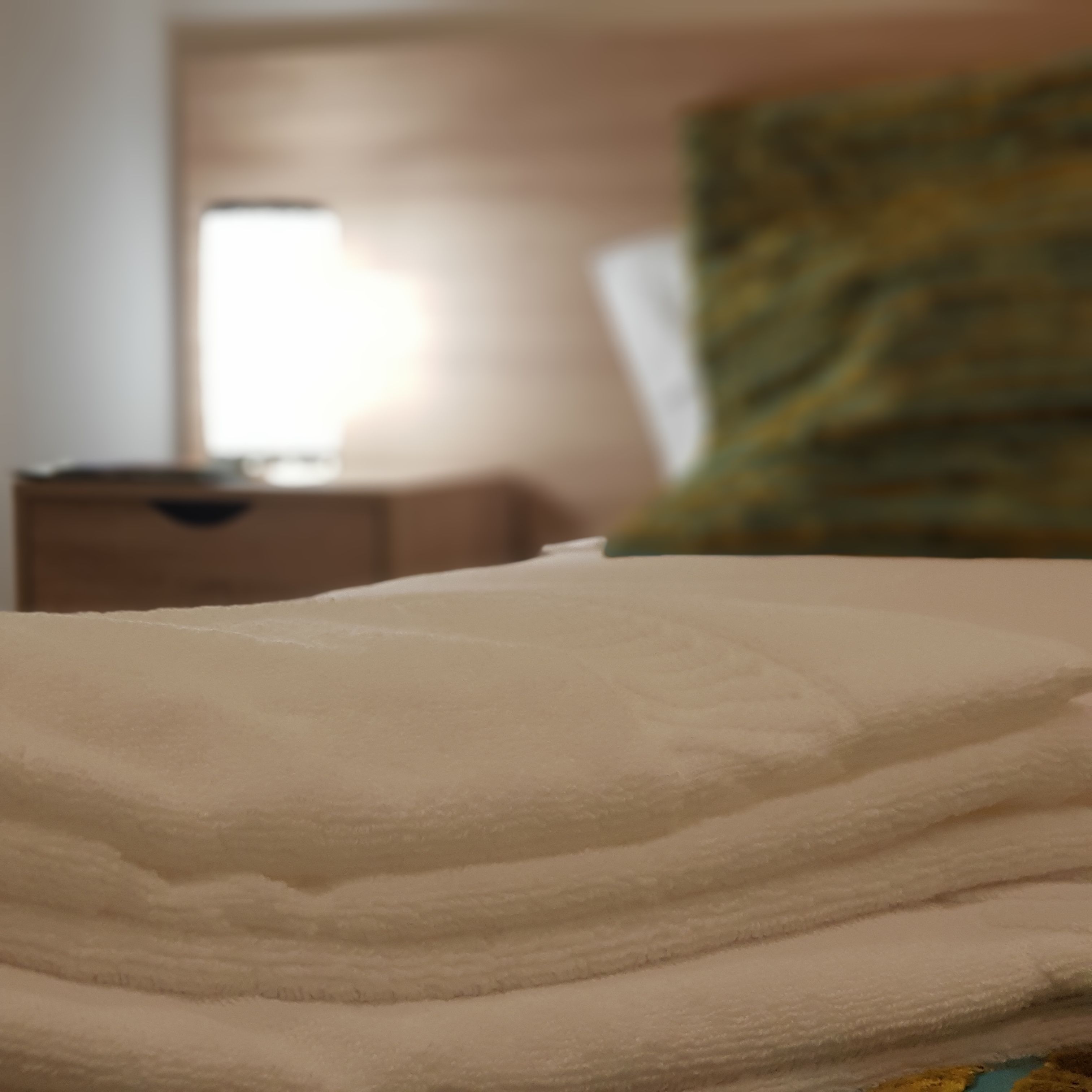 A bed with a white blanket, a wooden nightstand, and a green pillow in a hotel room.