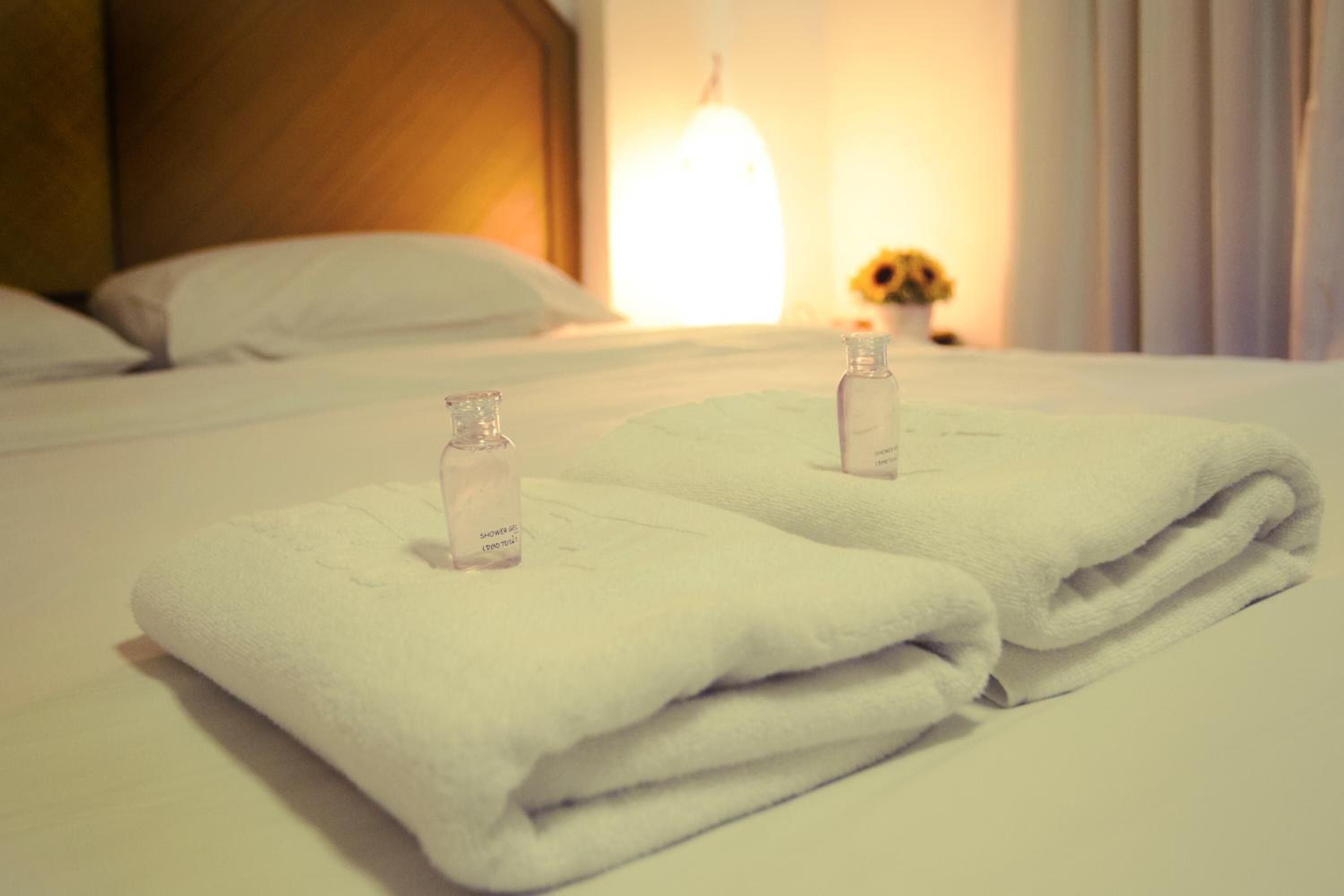 Una cama bien hecha con dos toallas blancas dobladas y dos pequeños frascos de gel de ducha.