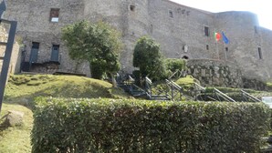 Un edificio histórico de piedra con una torre redonda, una escalera que conduce a la entrada y un asta de bandera con banderas.