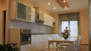 Una cocina moderna con armarios blancos, horno empotrado y comedor con mesa y sillas.