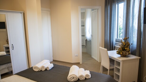Habitación de hotel con cama, escritorio y silla. Hay toallas sobre la cama y un florero con flores en el escritorio.