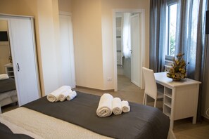 Habitación de hotel con cama, escritorio y silla. Hay toallas sobre la cama y un florero con flores en el escritorio.