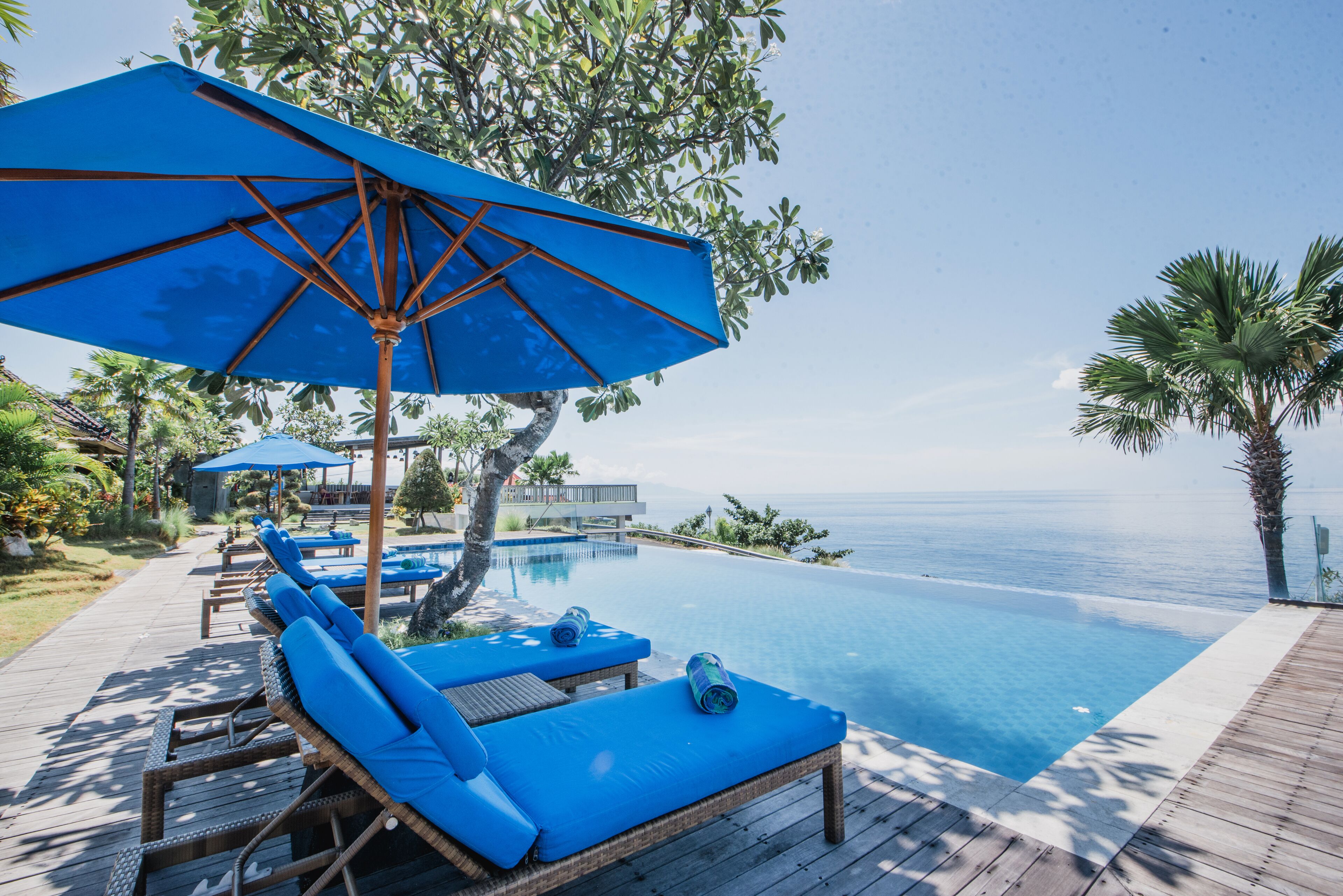 Ein Poolbereich mit Liegestühlen und Sonnenschirmen mit Blick auf das klare, blaue Meer.