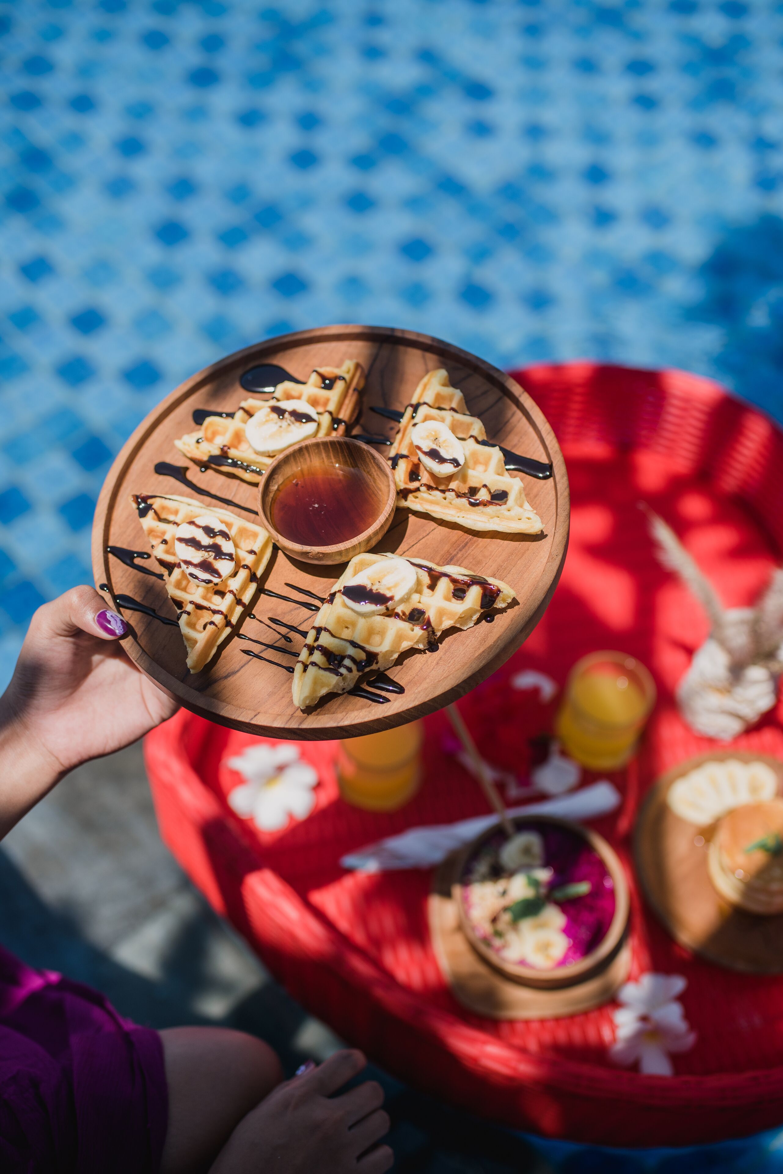 A wooden tray with waffles and syrup, held by a person.