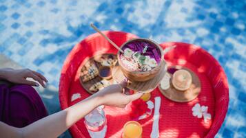 A person holding a wooden bowl with a purple drink, a red tray with food and drinks, and a blue patterned tablecloth.