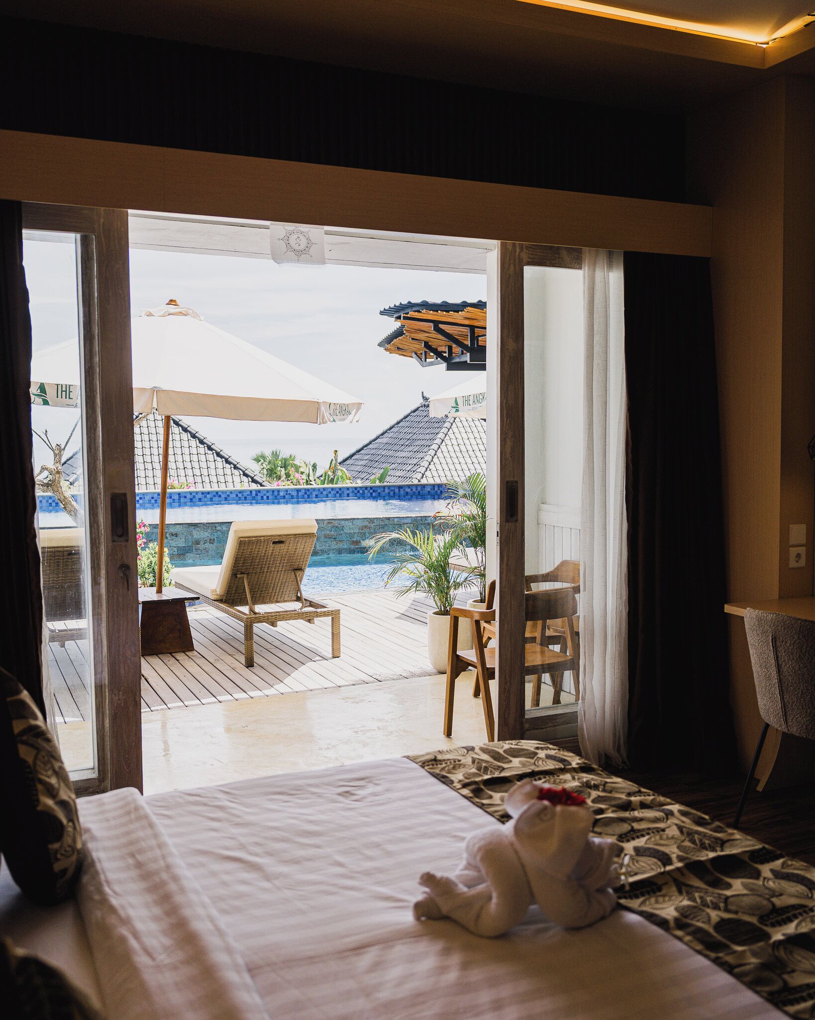 Quarto de hotel com uma cama, vista para a piscina e uma cadeira junto à piscina.